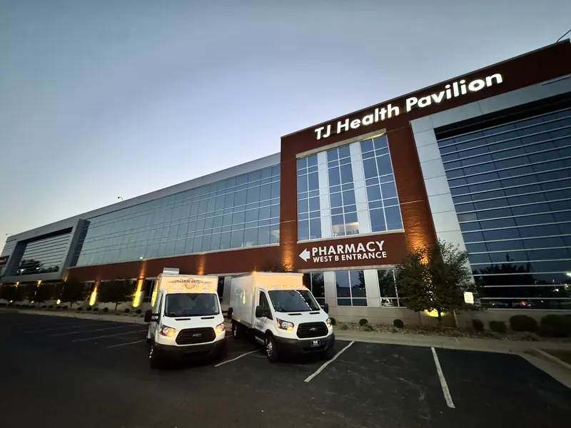 Two Shine Brite box trucks parked in front of a hospital pavilion at dusk
