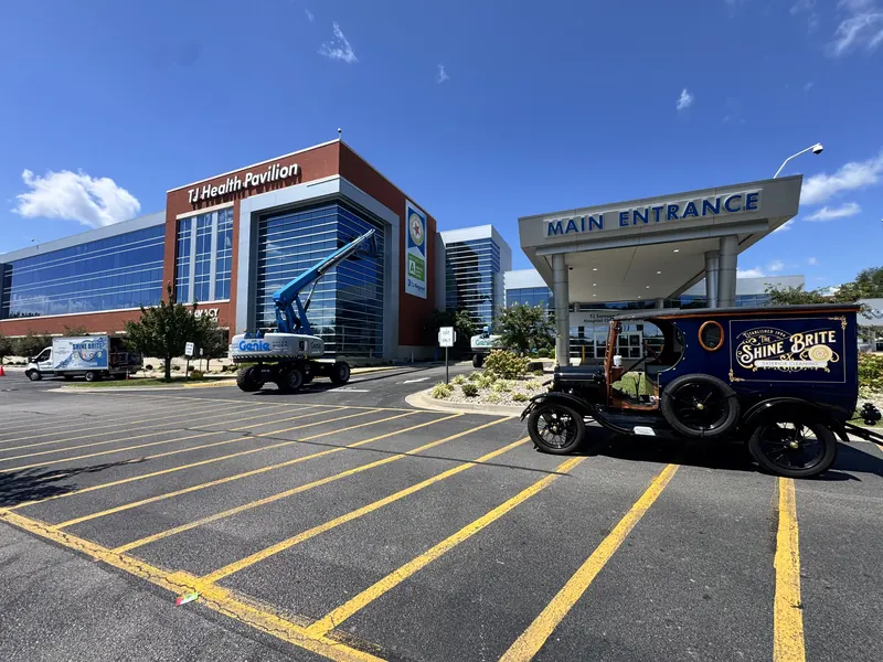 Shine Brite Model T work truck parked at a hospital main entrance while a lift crew cleans the building